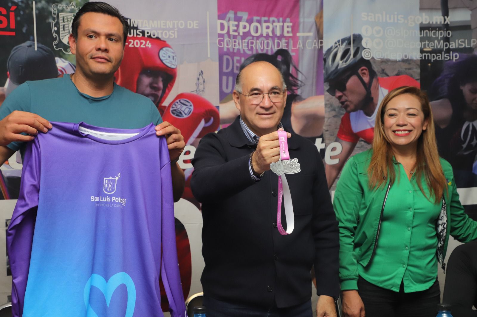 Fotografía del alcalde y el director de deporte mostrando las playeras y las medallas del maratón