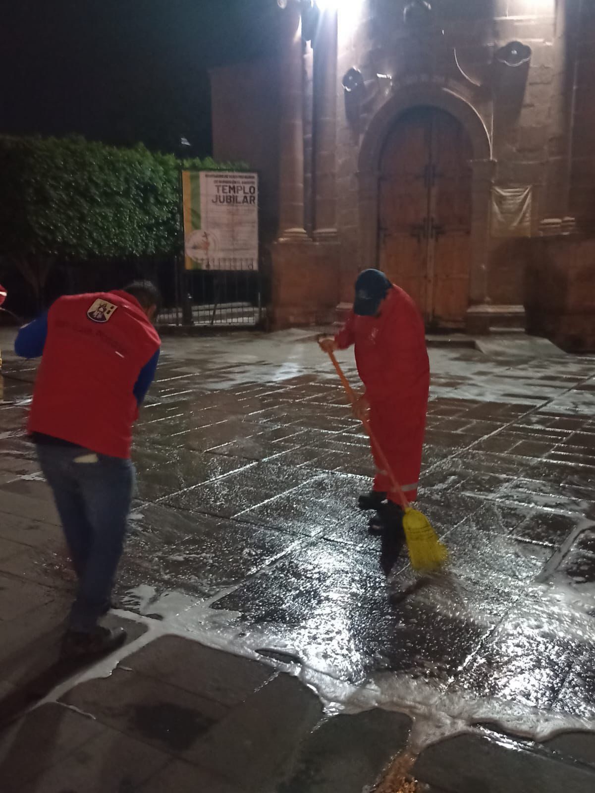 Fotografía de una persona barriendo una plaza pública de noche